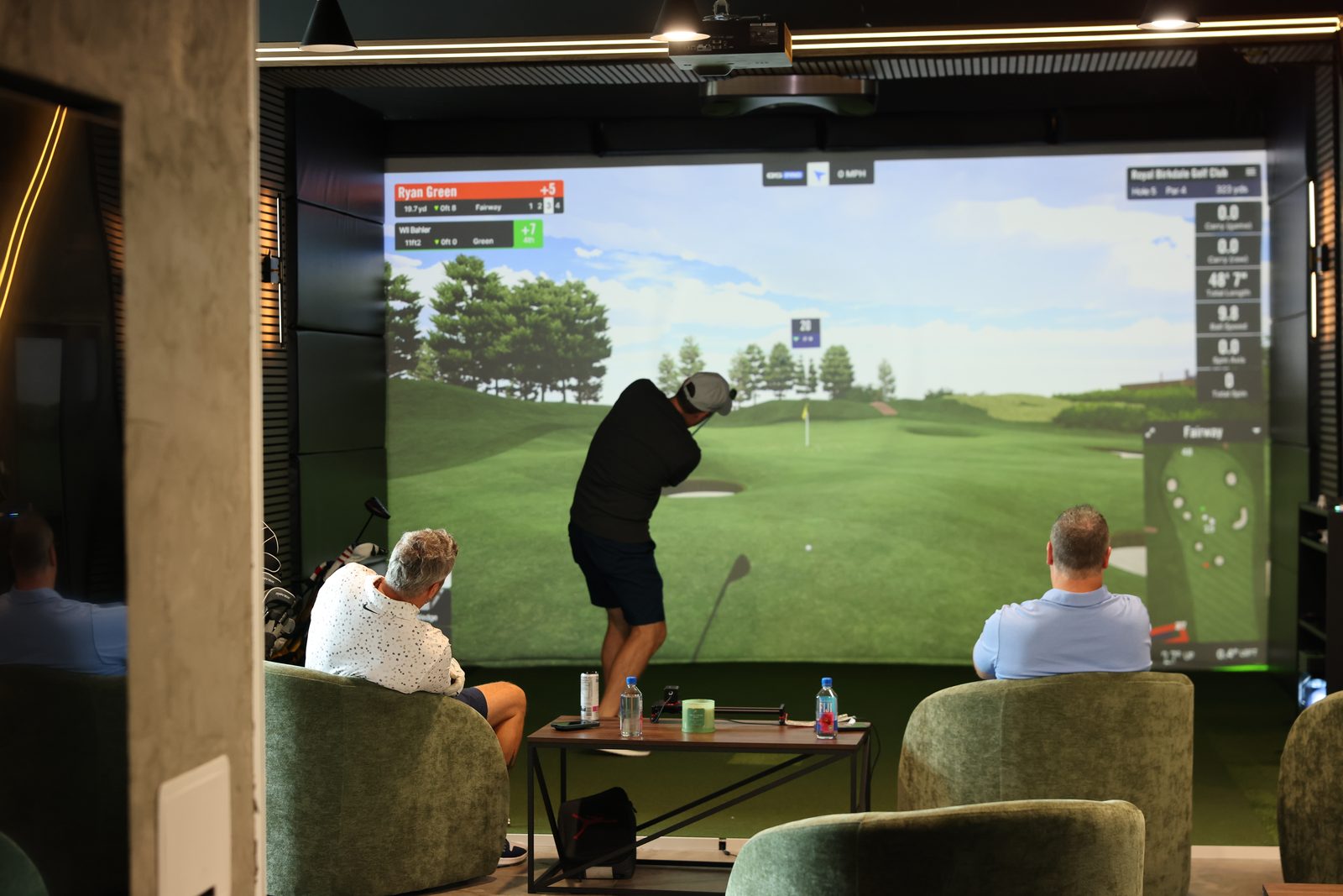 A player mid-swing at Royal Birkdale while two others watch from the lounge